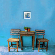 Open Your Eyes - Heart Art Original - on blue wall - in area with small wooden table and wooden terrace chairs.
